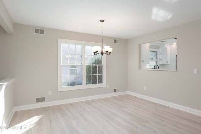 unfurnished dining area featuring an inviting chandelier and light hardwood / wood-style flooring