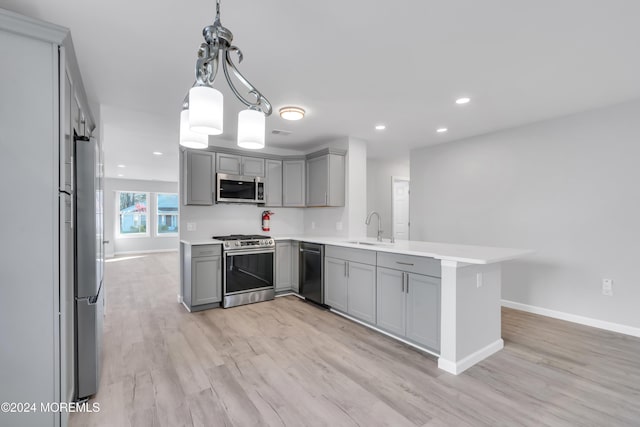 kitchen with gray cabinetry, kitchen peninsula, pendant lighting, appliances with stainless steel finishes, and light wood-type flooring