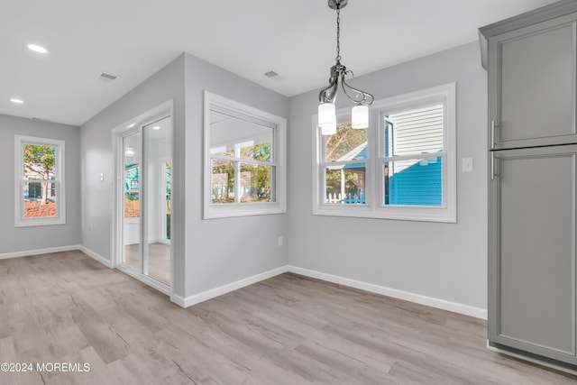 unfurnished dining area featuring plenty of natural light, a notable chandelier, and light hardwood / wood-style flooring