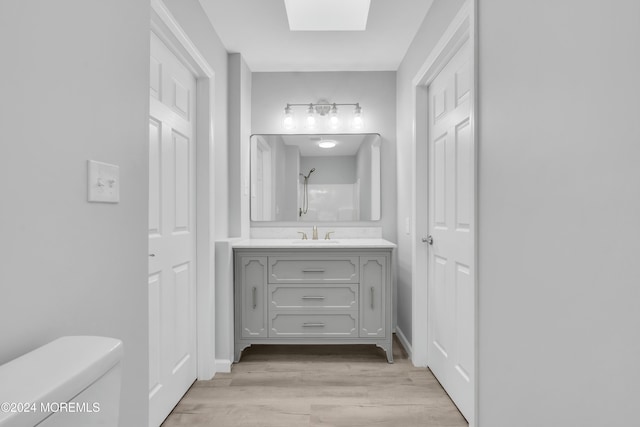 bathroom featuring a skylight, walk in shower, toilet, vanity, and hardwood / wood-style flooring