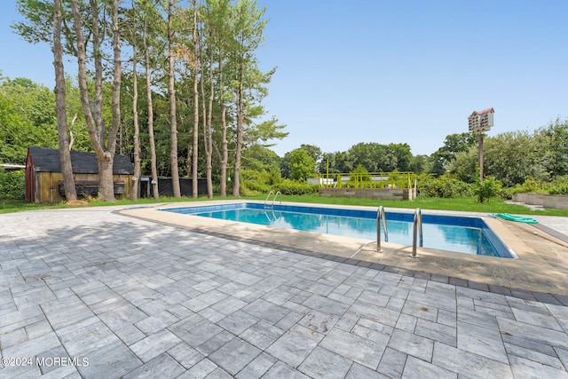 view of swimming pool featuring a shed and a patio area