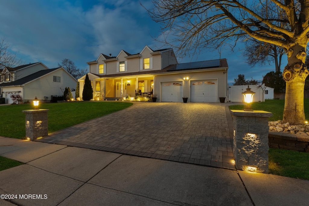 view of front of property with a lawn, solar panels, a garage, and covered porch