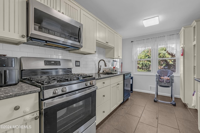 kitchen featuring backsplash, sink, light tile patterned floors, appliances with stainless steel finishes, and cream cabinetry