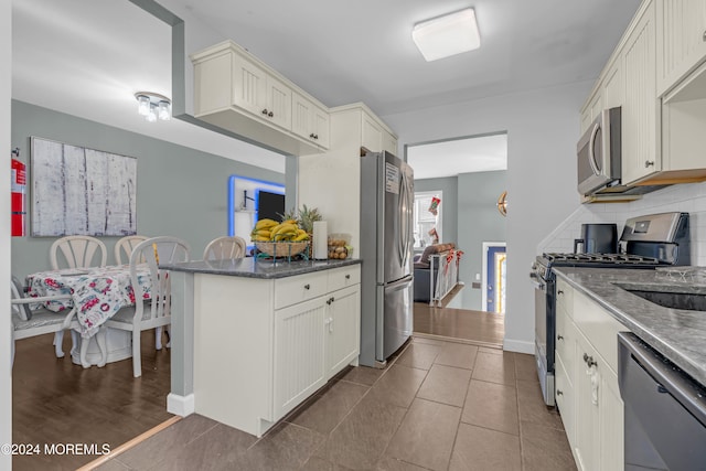 kitchen featuring stainless steel appliances, dark hardwood / wood-style flooring, kitchen peninsula, dark stone counters, and white cabinets