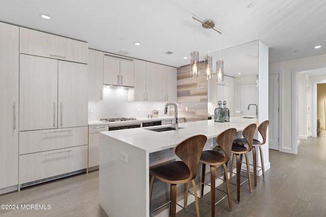 kitchen featuring a kitchen breakfast bar, sink, light hardwood / wood-style flooring, tasteful backsplash, and decorative light fixtures