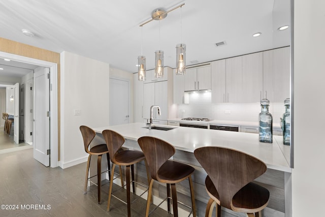 kitchen featuring pendant lighting, a breakfast bar, backsplash, sink, and hardwood / wood-style flooring