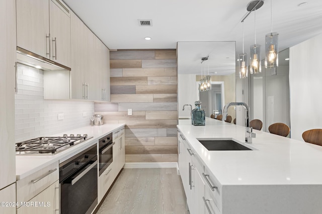 kitchen featuring hanging light fixtures, sink, wooden walls, light hardwood / wood-style floors, and stainless steel appliances