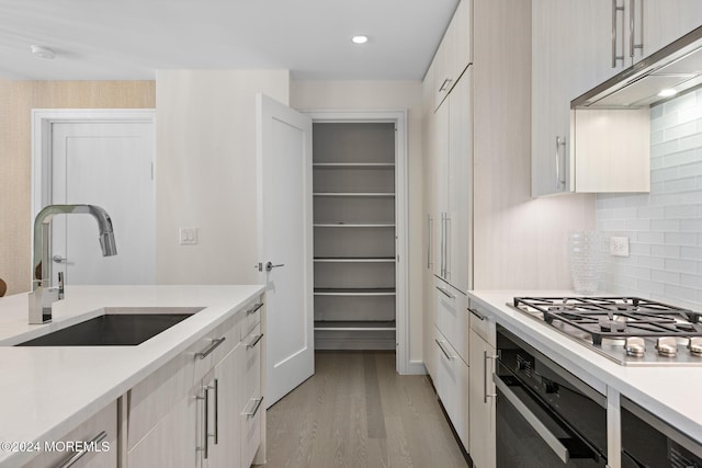 kitchen featuring sink, backsplash, stainless steel gas stovetop, black oven, and light wood-type flooring