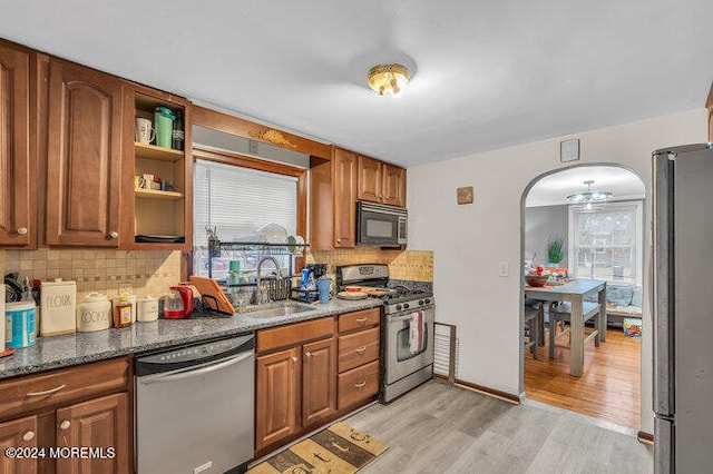 kitchen featuring sink, stainless steel appliances, tasteful backsplash, light hardwood / wood-style flooring, and dark stone counters