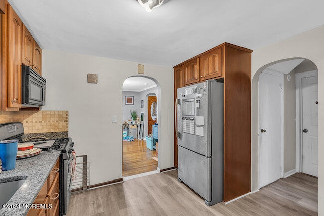 kitchen featuring decorative backsplash, light stone countertops, appliances with stainless steel finishes, and light hardwood / wood-style flooring