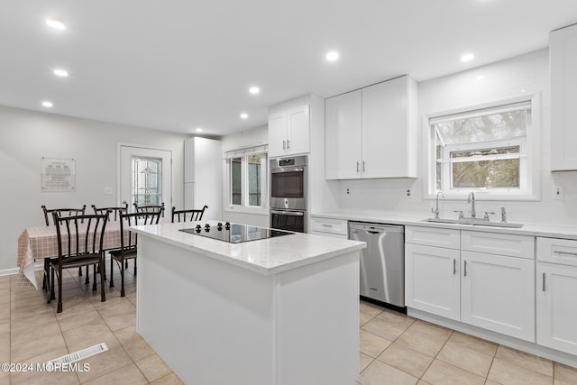 kitchen featuring stainless steel appliances, sink, light tile patterned floors, white cabinets, and a kitchen island