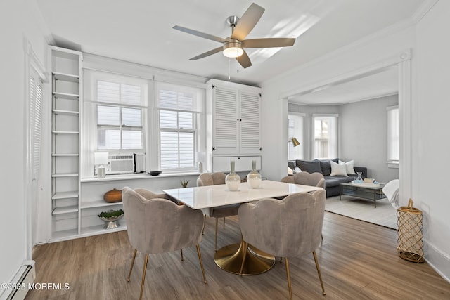 dining area featuring a wealth of natural light, a baseboard heating unit, wood finished floors, and crown molding