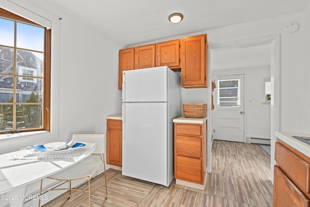 kitchen with light wood-style flooring, freestanding refrigerator, light countertops, a baseboard heating unit, and crown molding