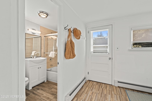 doorway with baseboard heating, light wood-style flooring, and ornamental molding