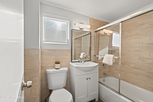 full bathroom featuring vanity, tile walls, toilet, and bath / shower combo with glass door