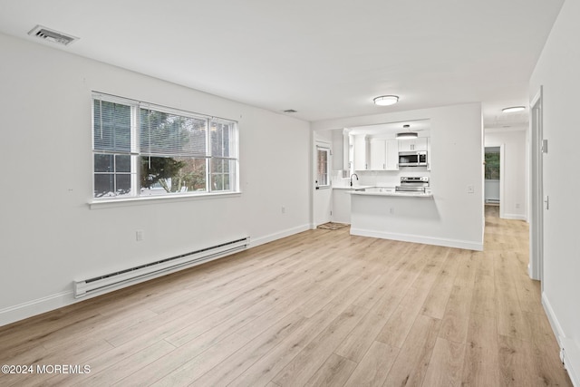 unfurnished living room with sink, baseboard heating, and light hardwood / wood-style flooring