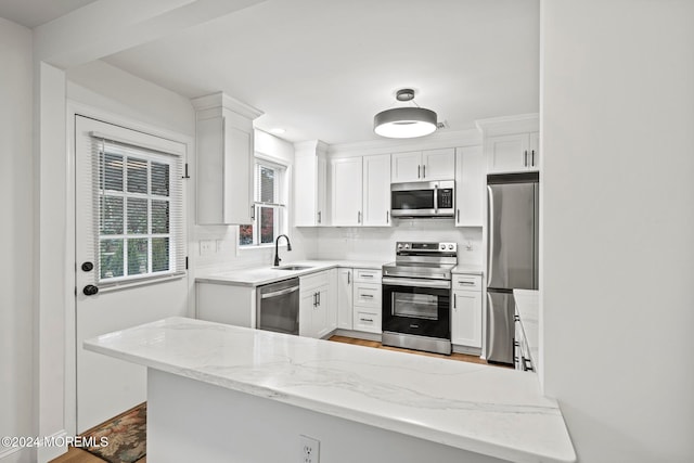 kitchen with white cabinets, sink, light stone countertops, kitchen peninsula, and stainless steel appliances