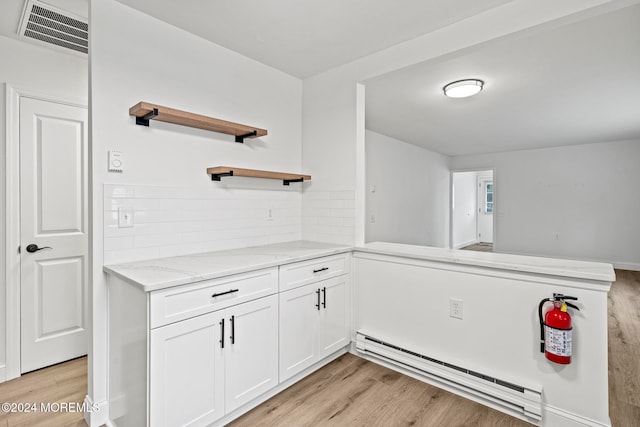 kitchen with white cabinetry, a baseboard radiator, light stone counters, kitchen peninsula, and light hardwood / wood-style floors