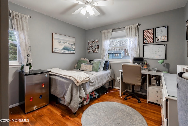 bedroom with hardwood / wood-style floors, ceiling fan, fridge, and multiple windows