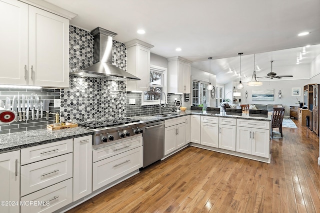 kitchen featuring wall chimney range hood, sink, hanging light fixtures, kitchen peninsula, and stainless steel appliances