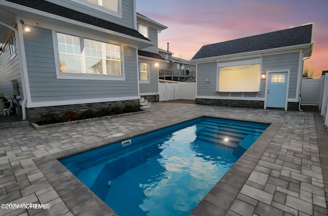 pool at dusk featuring an outdoor structure and a patio