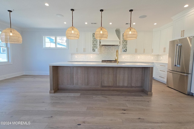 kitchen with premium range hood, a kitchen island with sink, sink, stainless steel fridge, and white cabinetry