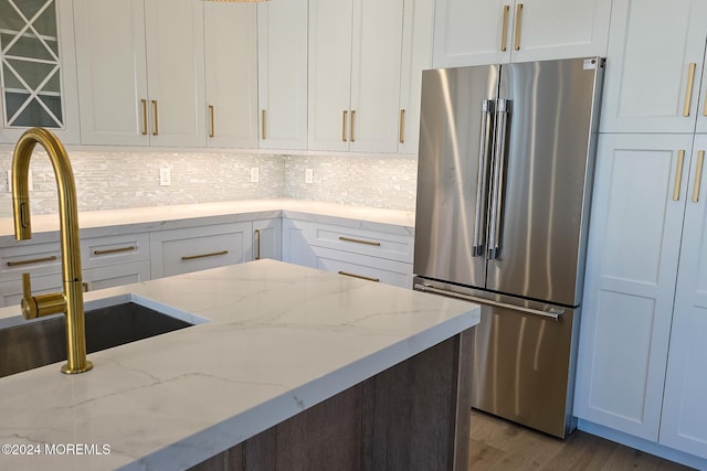 kitchen featuring white cabinets, light stone counters, high end fridge, and sink