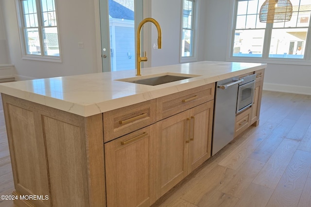 kitchen featuring light brown cabinets, sink, an island with sink, light hardwood / wood-style floors, and stainless steel appliances