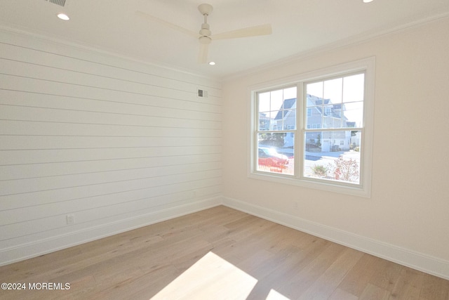 spare room with ceiling fan, crown molding, light hardwood / wood-style floors, and wood walls