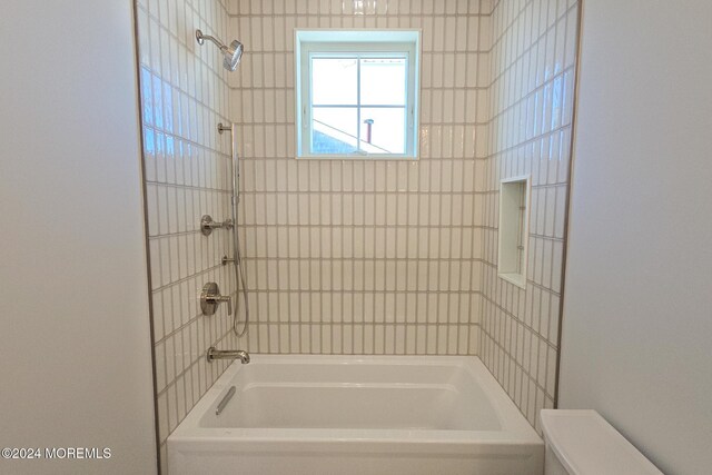 bathroom featuring tiled shower / bath combo and toilet