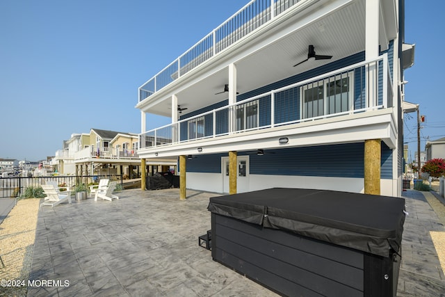 rear view of house featuring a patio area, ceiling fan, a balcony, and a hot tub