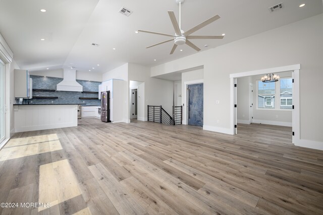 unfurnished living room with ceiling fan with notable chandelier and light wood-type flooring