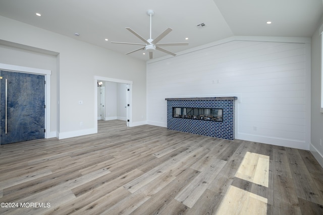 unfurnished living room with ceiling fan, a tiled fireplace, light hardwood / wood-style flooring, and vaulted ceiling