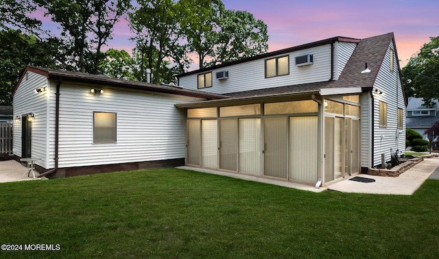 back house at dusk with a sunroom, a yard, and a wall mounted AC