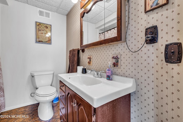 bathroom with walk in shower, a drop ceiling, vanity, and toilet