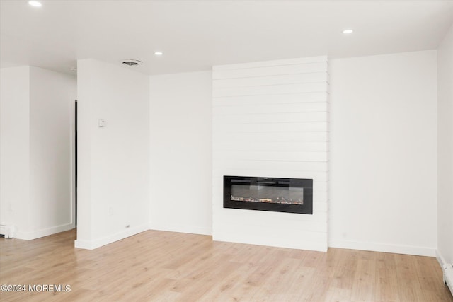 unfurnished living room with a large fireplace, light wood-type flooring, and a baseboard heating unit