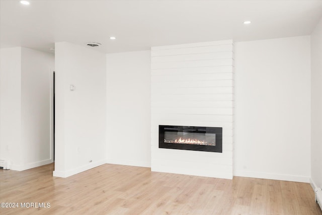 unfurnished living room featuring a large fireplace, light wood-type flooring, and baseboard heating