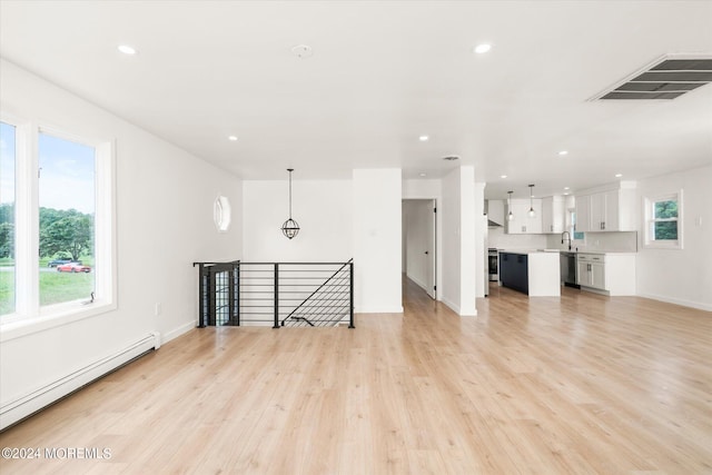 unfurnished living room featuring light wood-type flooring, a baseboard heating unit, and sink