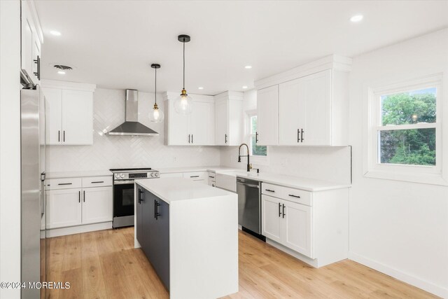 kitchen featuring a center island, wall chimney range hood, decorative light fixtures, appliances with stainless steel finishes, and light wood-type flooring