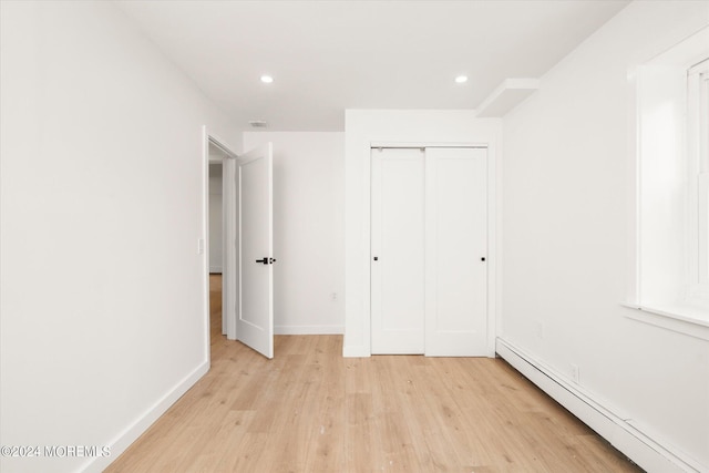 unfurnished bedroom with a baseboard radiator, a closet, and light hardwood / wood-style floors