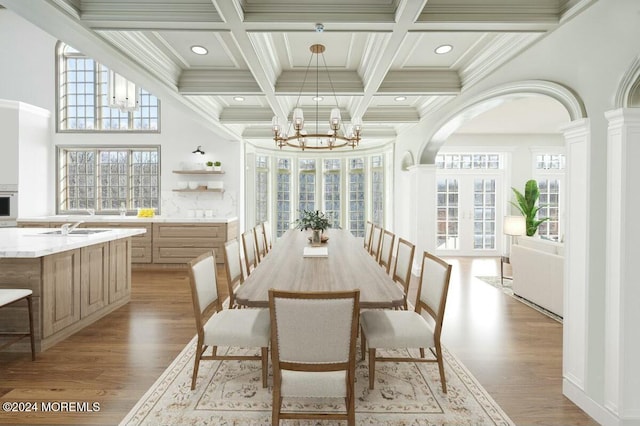 dining area with beamed ceiling, light wood-type flooring, a notable chandelier, and sink