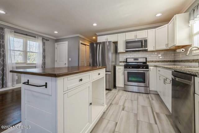 kitchen with white cabinets, crown molding, sink, appliances with stainless steel finishes, and a kitchen island