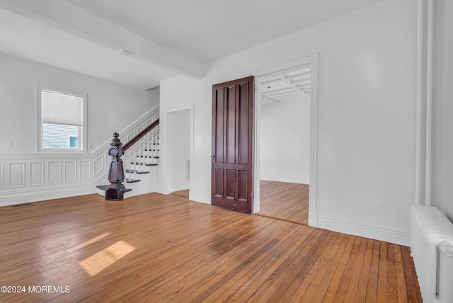 empty room featuring beam ceiling, hardwood / wood-style flooring, and radiator