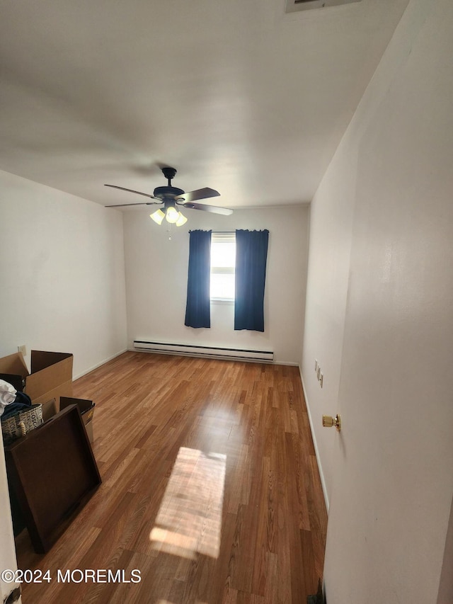 empty room with hardwood / wood-style flooring, ceiling fan, and a baseboard heating unit