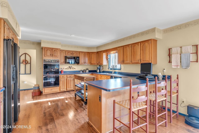 kitchen with kitchen peninsula, light wood-type flooring, sink, black appliances, and a breakfast bar area