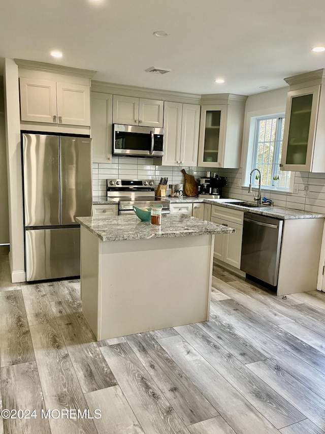 kitchen featuring light wood-type flooring, light stone counters, stainless steel appliances, sink, and a kitchen island