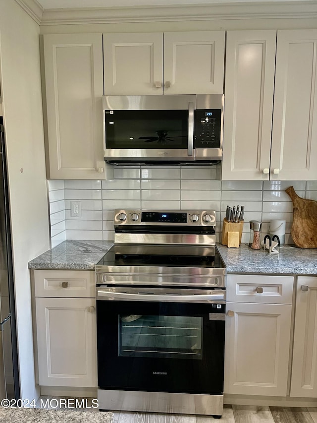 kitchen featuring light hardwood / wood-style flooring, decorative backsplash, appliances with stainless steel finishes, light stone counters, and white cabinetry