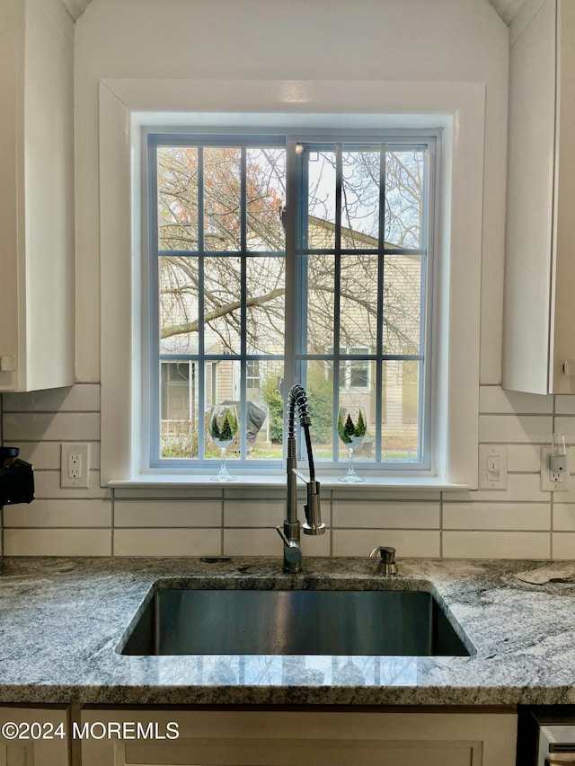 interior details featuring decorative backsplash, light stone counters, and sink