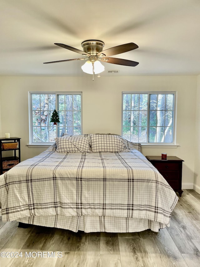 bedroom with ceiling fan, wood-type flooring, and multiple windows