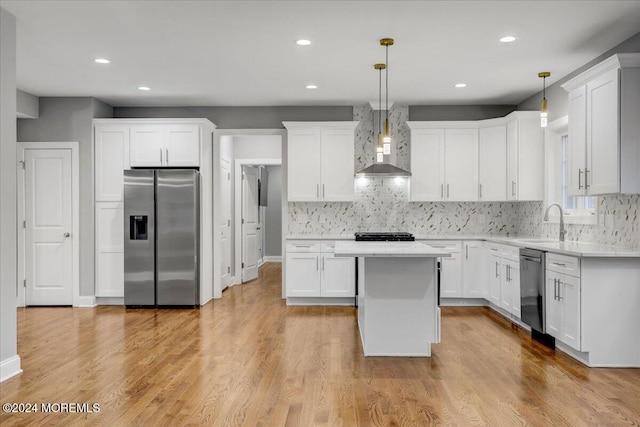 kitchen featuring pendant lighting, light wood-type flooring, wall chimney range hood, and appliances with stainless steel finishes